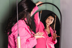 Woman in pink outfit looks at herself in the mirror. What she says to herself about herself shapes her perspective of who she is.